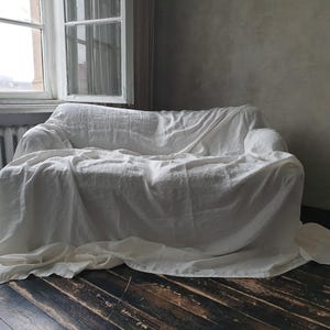 May include: A white linen sofa cover draped over a couch, creating a simple and elegant look.