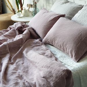 May include: A bed with a dusty rose linen duvet cover and two dusty rose linen pillowcases. A white linen pillowcase is visible under the dusty rose pillowcases.