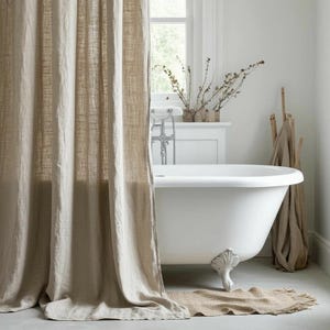 May include: A neutral-toned bathroom scene featuring a white clawfoot bathtub, a beige linen shower curtain, and a matching bath mat. The room is bright with natural light from a window, and includes decorative branches.