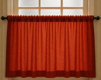 May include: A burnt orange window curtain hangs in front of a window with a frosted glass pane. The curtain is made of a textured fabric and is gathered at the top. The curtain rod is dark brown.