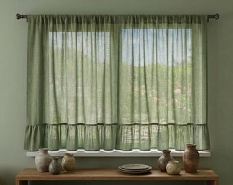 May include: A pair of sage green semi-sheer curtains featuring a rod pocket top and a ruffled bottom hem. The curtains are hung on a dark metal rod over a window, allowing soft light to filter through the fabric into the interior space.