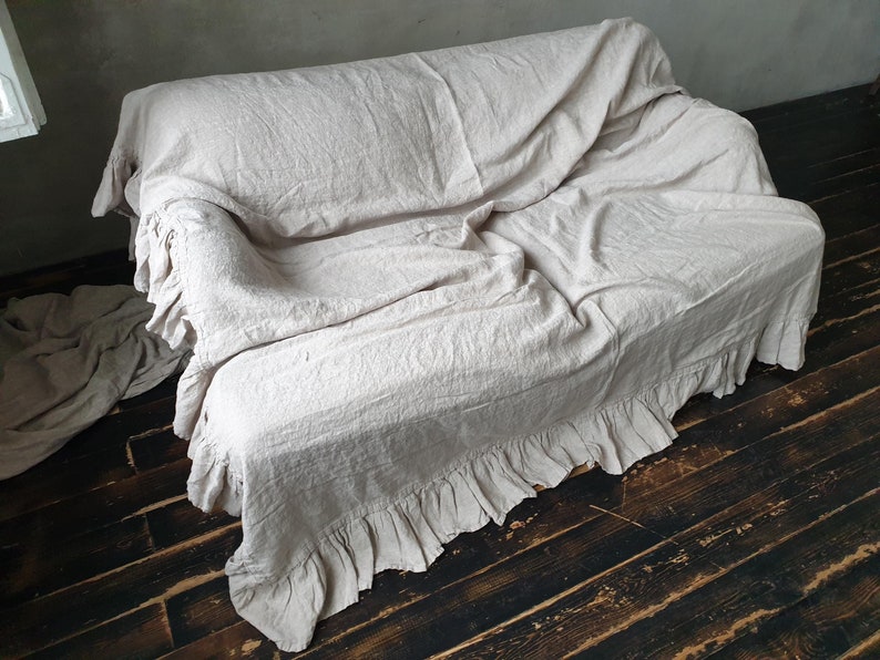 May include: A cream-colored linen sofa throw with a ruffled edge. The throw is draped over a sofa and has a relaxed, casual look.