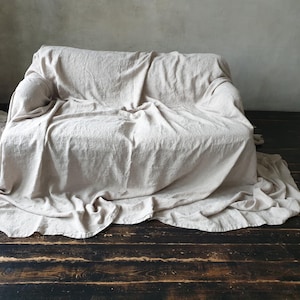 May include: A white linen throw blanket draped over a couch. The blanket is textured and has a natural, rustic look.