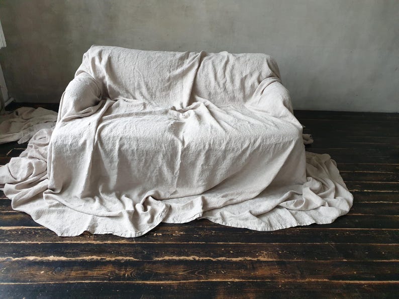 May include: A white linen throw blanket draped over a couch. The blanket is textured and has a natural, rustic look.