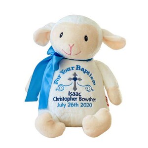 May include: A plush lamb toy with a blue ribbon around its neck. The lamb is white with beige accents and has embroidered text that reads "For Your Baptism" and the name "Isaac Christopher Bowsher" with the date "July 26th 2020".