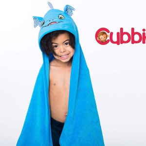 May include: A child wearing a blue hooded towel with a monster face design. The towel is a vibrant blue colour and features a monster face on the hood with striped accents. The Cubbies logo is visible in the upper right corner.