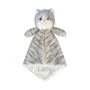 May include: A gray and white plush cat security blanket. The cat has a striped pattern, pink nose, and the name "Lucy" embroidered on the bottom. The blanket is designed for babies and young children.