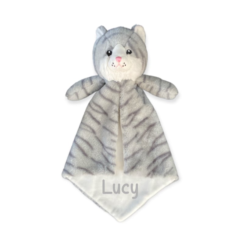 May include: A gray and white plush cat security blanket. The cat has a striped pattern, pink nose, and the name "Lucy" embroidered on the bottom. The blanket is designed for babies and young children.