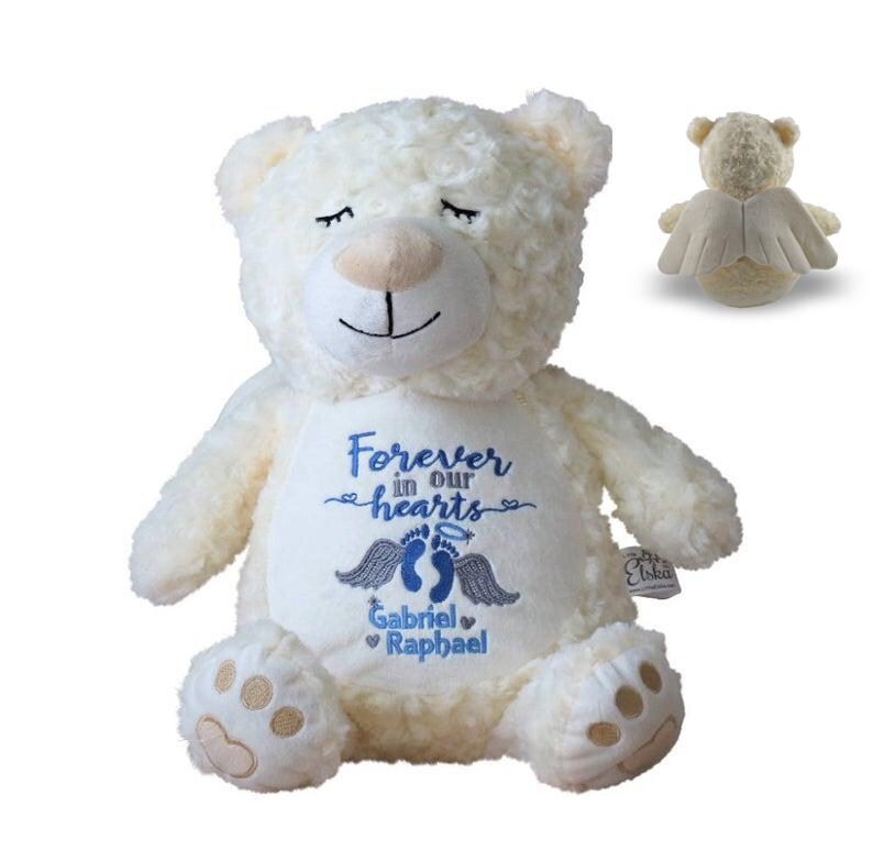 May include: Cream-colored plush teddy bear with embroidered text "Forever in our hearts" and the names Gabriel and Raphael. The bear has closed eyes and a small angel wing design on the back. A second bear with angel wings is also shown.