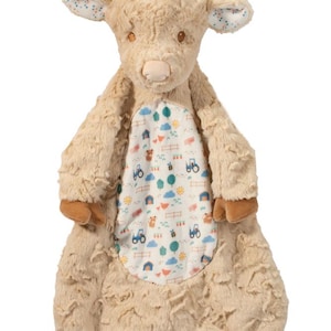 Pu&ograve; includere: Un peluche di mucca delle Highlands color beige con una pancia fantasia. La mucca ha zoccoli, corna e un ciuffo di capelli marroni. La pancia presenta una scena di fattoria con trattori, recinzioni e alberi.