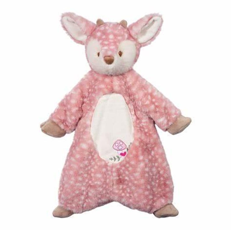 Pu&ograve; includere: Un giocattolo di peluche rosa a forma di cervo con macchie bianche, grandi orecchie e piccole corna. Il cervo ha una pancia bianca con un design ricamato a forma di fungo e cuore. Gli zoccoli e il naso del giocattolo sono marroni.
