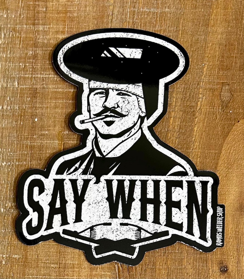 May include: Black and white sticker featuring a stylized illustration of a welder with a mustache, wearing a welding helmet and smoking a cigarette. The text "SAY WHEN" is prominently displayed below the image. The sticker has a distressed, vintage look.