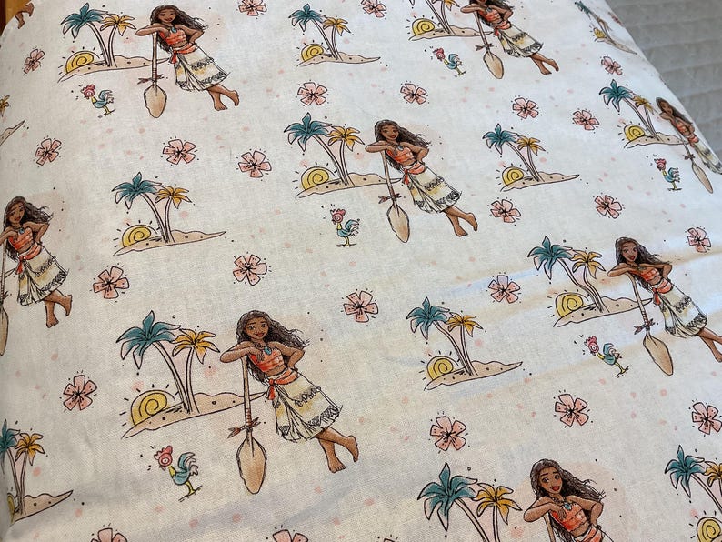 May include: White fabric with a repeating pattern of a cartoon character holding a paddle, palm trees, flowers, and roosters. The character is wearing a brown and orange outfit.