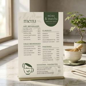 Peut inclure: Un panneau de menu rectangulaire vertical pour le café mino & matcha avec un fond crème et des accents vert foncé. Le menu liste des boissons chaudes, froides, des classiques, des pâtisseries et des favoris saisonniers avec des prix en dollars.