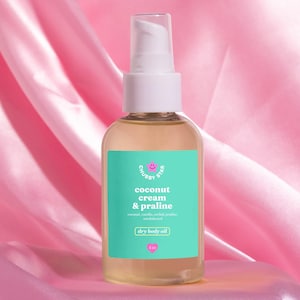 May include: A clear glass bottle with a white pump top filled with a light yellow liquid. The bottle has a turquoise label with the text "Chubby Star" and "coconut cream & praline" in pink text. The label also says "dry body oil" and "4 oz".