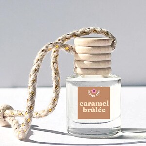 May include: A clear glass bottle with a wooden cap and a brown label that says "caramel brûlée" and "Chubby Star". The bottle is hanging from a white and gold rope.
