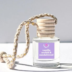 May include: A clear glass bottle with a wooden lid and a purple label that says "Chubby Star" and "vanilla orchid & sandalwood". The bottle is hanging from a white and gold rope.