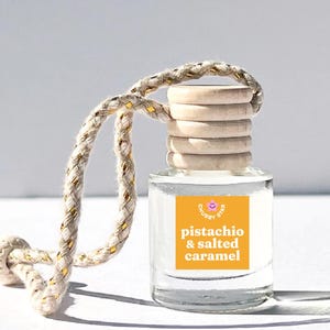 May include: A clear glass bottle with a wooden cap and a yellow label that says "pistachio & salted caramel" and "Chubby Star". The bottle is hanging from a white and gold rope.