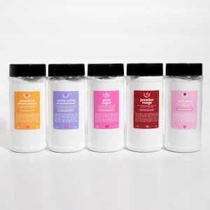 May include: Five white plastic jars with black lids and labels. The labels have different colored backgrounds and text. The text on the labels reads "pistachio & salted caramel", "vanilla orchid & sandalwood", "pink sugar", "jasmine rouge", and "only you".