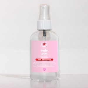 May include: A clear glass bottle with a pink label that says "Only You" in white text. The label also says "Pink pepper, amber, citrus, sandalwood" and "Room & Linen Spray". The bottle has a white spray nozzle and is sitting on a white surface.