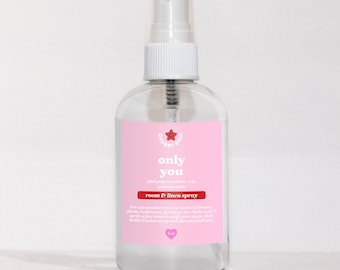 May include: A clear glass bottle with a pink label that says "Only You" in white text. The label also says "Pink pepper, amber, citrus, sandalwood" and "Room & Linen Spray". The bottle has a white spray nozzle and is sitting on a white surface.