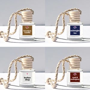 May include: Four glass bottles with wooden stoppers and string hangers. Each bottle has a different colored label with text. The labels read "bourbon vanilla", "midnight ice", "barber shop", and "teak & mahogany".