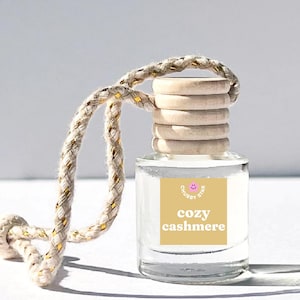 May include: A clear glass bottle with a wooden cap and a beige string hanging from it. The bottle has a label that says "Chubby Star" and "cozy cashmere".