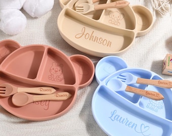 Op de afbeelding: Drie kleurrijke, verdeelde siliconen borden in de vorm van beren met bijpassende houten lepels en vorken. De borden zijn gepersonaliseerd met de namen "Johnson", "Ramsey" en "Lauren".