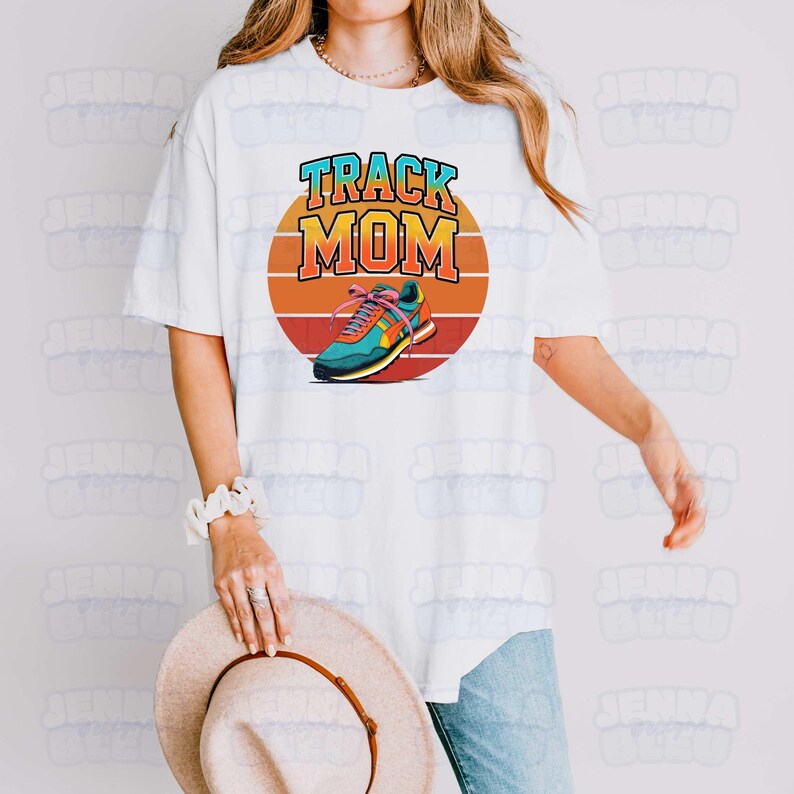 Peut inclure: T-shirt blanc avec un graphisme color&eacute; qui dit "Track Mom". Le graphisme pr&eacute;sente une chaussure de course en bleu sarcelle, orange et jaune, sur fond de coucher de soleil. Le t-shirt est de style d&eacute;contract&eacute;.