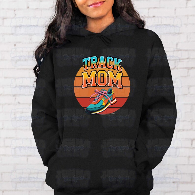 Peut inclure: Sweat &agrave; capuche noir avec un graphisme color&eacute;. Le graphisme pr&eacute;sente les mots "TRACK MOM" en bleu et orange, avec un design de chaussure de course sur fond de coucher de soleil.