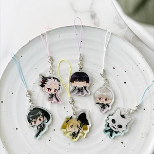 Op de afbeelding: Een verzameling van zeven anime-stijl acryl bedels met verschillende karakterontwerpen. Elke bedel heeft een unieke karakterillustratie, bevestigd aan een zilverkleurige sluiting en een gekleurd koord. De bedels worden gepresenteerd op een wit bord.