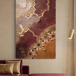 Peut inclure: Tableau abstrait avec un motif détaillé en bordeaux, or et beige. Le design incorpore des formes géométriques et des textures, créant une esthétique vintage. L'œuvre est affichée au-dessus d'un canapé bordeaux avec des coussins dorés.