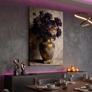 Könnte beinhalten: Ein Leinwanddruck eines Stilllebens mit einer goldenen Vase, gefüllt mit dunkelvioletten und rosa Blumen. Die Vase steht vor einem neutralen Hintergrund. Das Kunstwerk hängt über einem dunklen Holzschrank mit dekorativen Objekten und Kerzen.