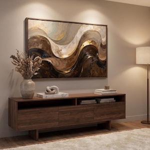 Op de afbeelding: Een rechthoekig wandkunstwerk met abstracte golvende lijnen in bruin-, crème- en goudtinten, ingelijst in donker hout. Het schilderij hangt boven een lang, laag houten mediameubel met drie lades en open vakken voor opslag.