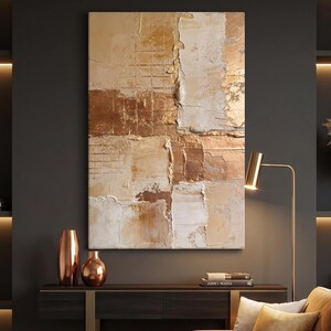 May include: Abstract textured wall art in shades of beige, cream, and bronze. The artwork features a cross-like design with a grid pattern and rough, layered textures. Two copper vases and a floor lamp are in the foreground.