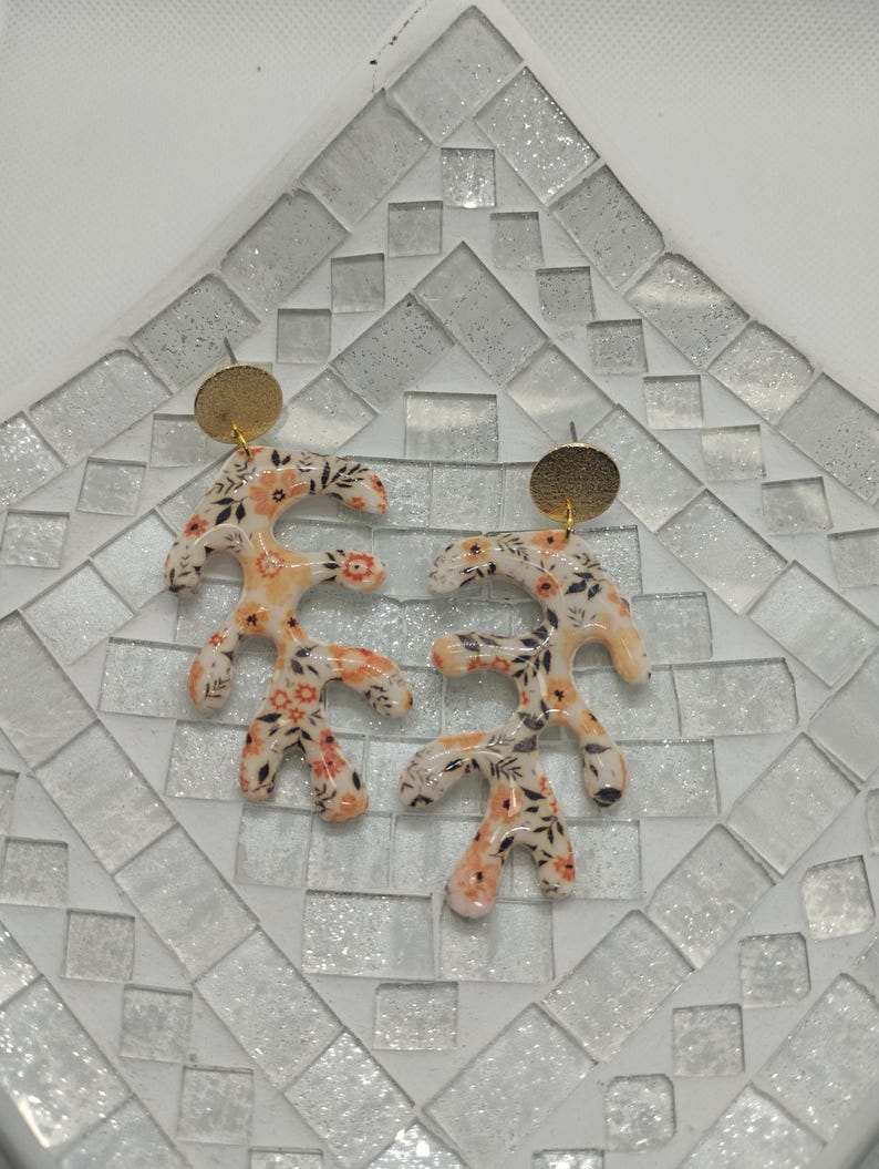 May include: A pair of floral patterned earrings with gold accents. The earrings are shaped like branches with small flowers and leaves.