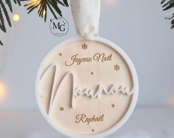 Könnte beinhalten: Ein runder Weihnachtsschmuck mit den Worten "Joyeux Noël" und "Maman" in einer dekorativen Schriftart. Der Schmuck hat einen weißen Rand und eine beige Mitte mit dem eingravierten Namen "Raphaël".