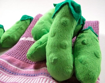 May include: Five plush green pickle toys with green felt tops, arranged on a pink and white striped towel.