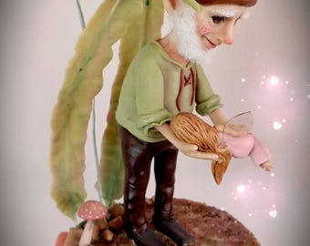 May include: A whimsical figurine of a fairy holding a small doll. The fairy wears a green shirt, brown pants, and a brown hat. The base is a wooden circle with a textured surface. A flower and mushroom are also present.