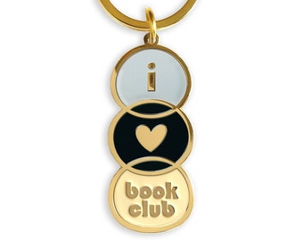 May include: Gold-tone keychain with three round charms. The top charm is white with the letter 'i' in black. The middle charm is black with a gold heart. The bottom charm is gold with the text 'book club' in black.