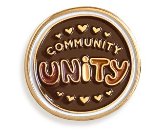 May include: A gold and brown enamel pin with a white border. The pin features the words "Community Unity" in a retro font with hearts around the text.