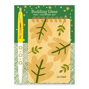 May include: A yellow pen with gold accents and a white body featuring a repeating sun and star design. The pen is next to a small spiral bound notepad with a wood-grain cover. The cover has a green and yellow leaf design and the word "notes" printed on the bottom. The background is green with gold stars.
