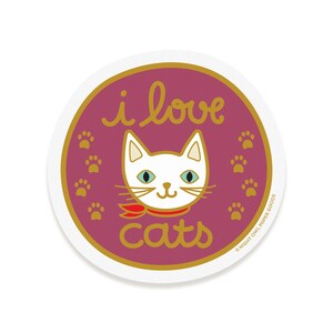 May include: A round sticker with a pink background and gold lettering. The sticker says "i love cats" with a white cat wearing a red scarf in the center. There are gold paw prints around the cat.