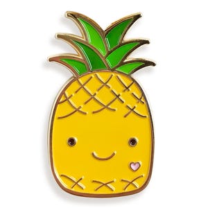 Puede incluir: Un pin de esmalte de color dorado con forma de piña con una cara sonriente y un pequeño corazón rosa. La piña tiene hojas verdes y un cuerpo amarillo con un patrón de cuadrícula marrón.