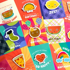 May include: A collection of colorful greeting cards with various food-themed illustrations and puns. The cards feature a taco, a pickle, a watermelon, a coconut, a pizza, a heart, a lemon, and a rainbow. The cards are perfect for birthdays and other special occasions.
