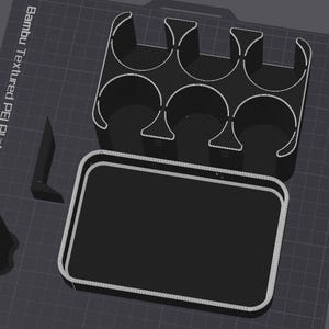 May include: A black 3D printed storage organizer featuring a rectangular tray base and a separate insert with six circular compartments. The components are displayed on a dark grid surface labeled Bambu Textured PEI Plate, including a small corner bracket.