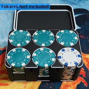 May include: A black poker chip case with six compartments, each holding stacks of poker chips. The chips are teal, white, and blue. The text "Tokens Not Included" is at the top of the case.