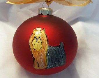 May include: A red Christmas bauble with a hand-painted Yorkshire Terrier on it. The bauble has a gold ribbon attached to the top.