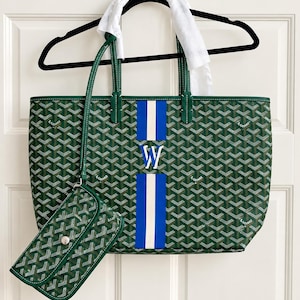 May include: A green tote bag with a repeating white and grey chevron pattern and a central vertical stripe in blue and white featuring the letter W. The bag includes a matching detachable pouch with a silver snap closure and green leather trim.