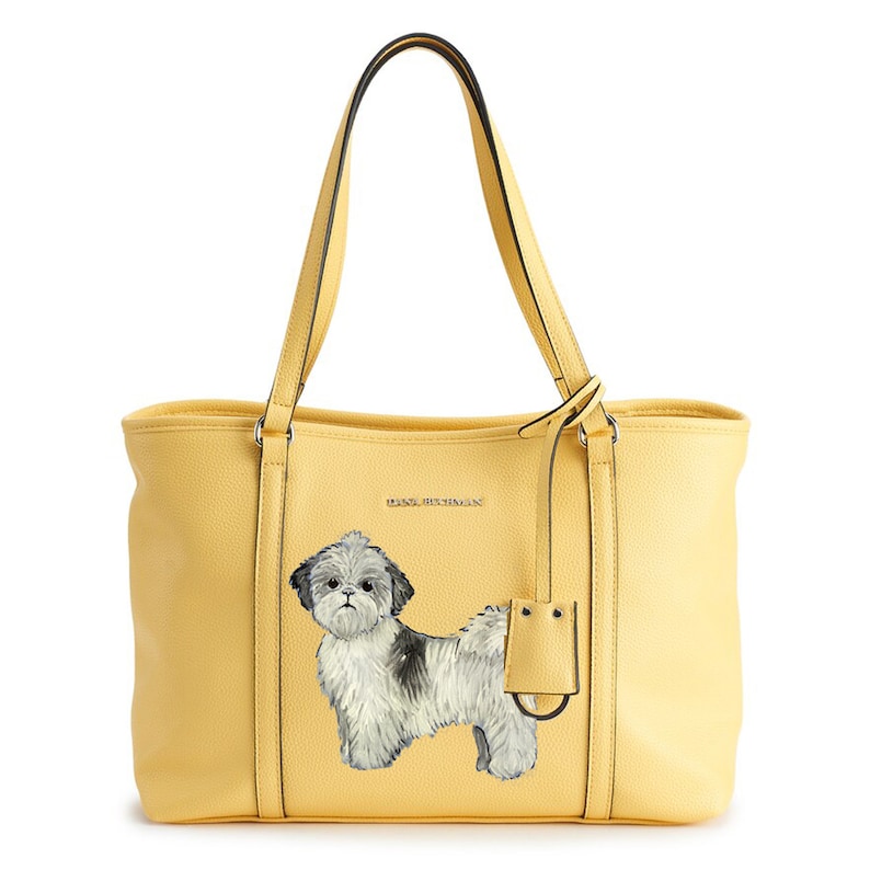 May include: A yellow tote bag with a black and white illustration of a Shih Tzu dog. The bag has a black leather handle and a silver metal tag with the text "Dana Buchman" on it.